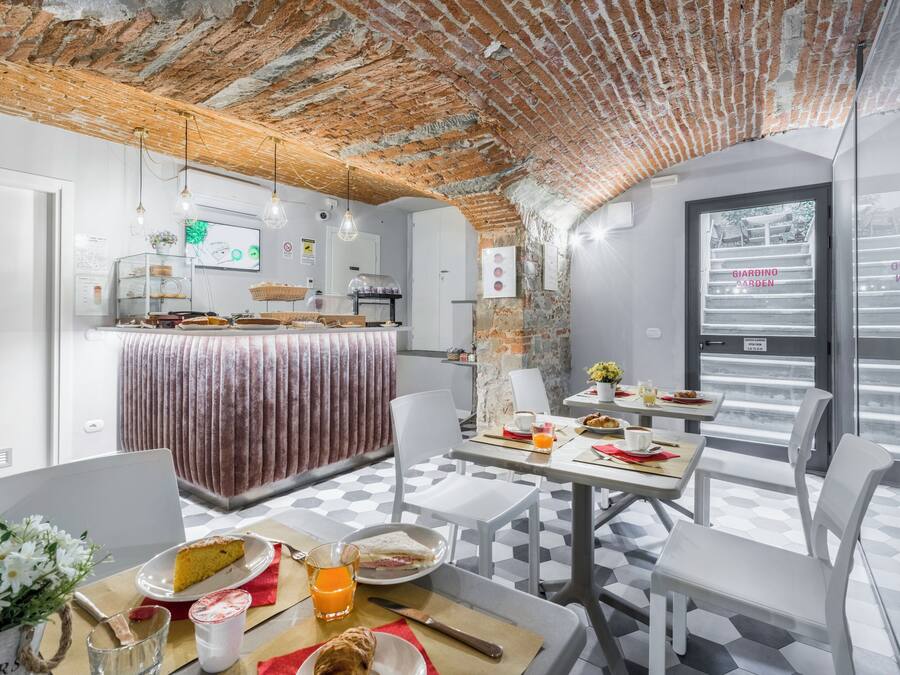 Un área de desayuno con techo de ladrillo, paredes blancas y piso de baldosas. Hay mesas con alimentos para el desayuno, sillas y una barra con una vitrina.