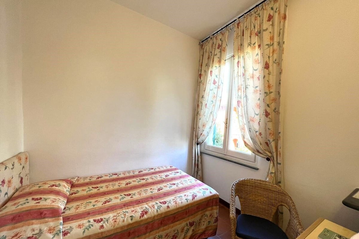 Ein Schlafzimmer mit Bett, einem Sessel und einem Fenster mit blumigen Vorhängen.