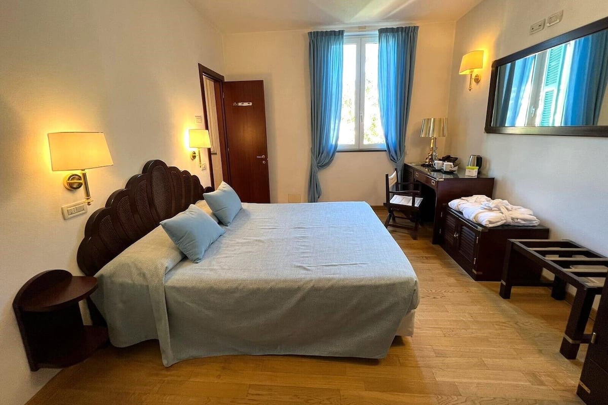 Ein Hotelzimmer mit einem großen Bett, einem Schreibtisch, einem Stuhl, einem Spiegel und einem Fenster mit Vorhängen.