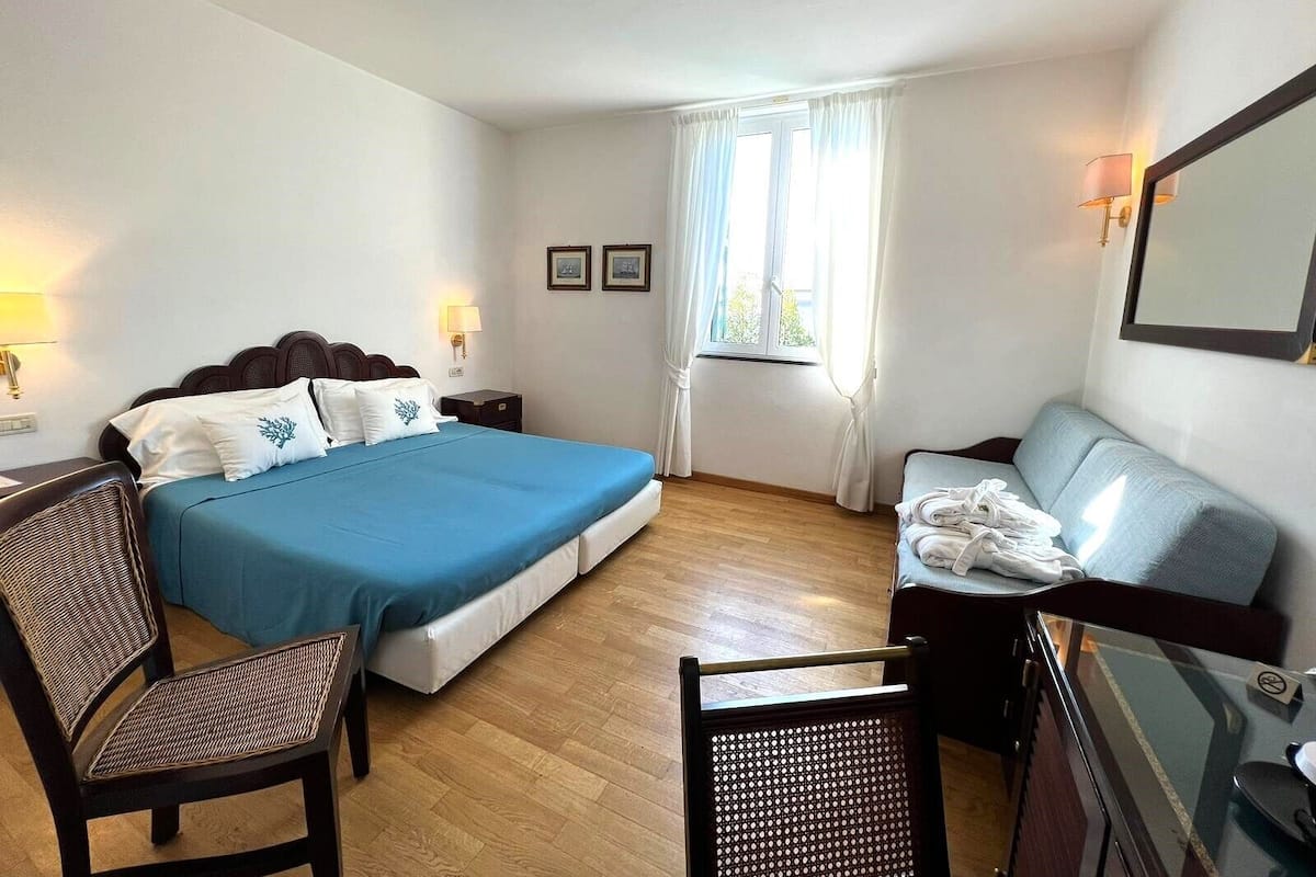 Ein Hotelzimmer mit Bett, Schreibtisch, Stuhl, Sofa und einem fenster mit Vorhängen.