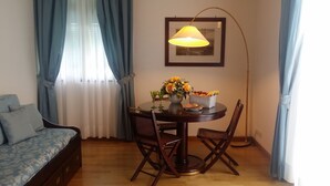 Uma área de refeições com uma mesa redonda, duas cadeiras, um vaso de flores e uma moldura na parede.