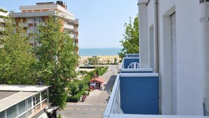 Vista de una calle costera con edificios, cielo despejado y una playa a lo lejos.