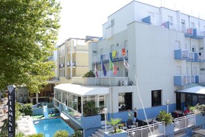Un hotel con piscina, mobiliario exterior y balcones con barandillas.