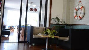 Un área de recepción con un sofá, una mesita con una planta y un flotador de salvavidas en la pared.