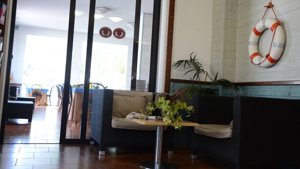 A reception area with a sofa, a small table with a plant, and a life ring on the wall. - Hotel Diamond (Rimini)