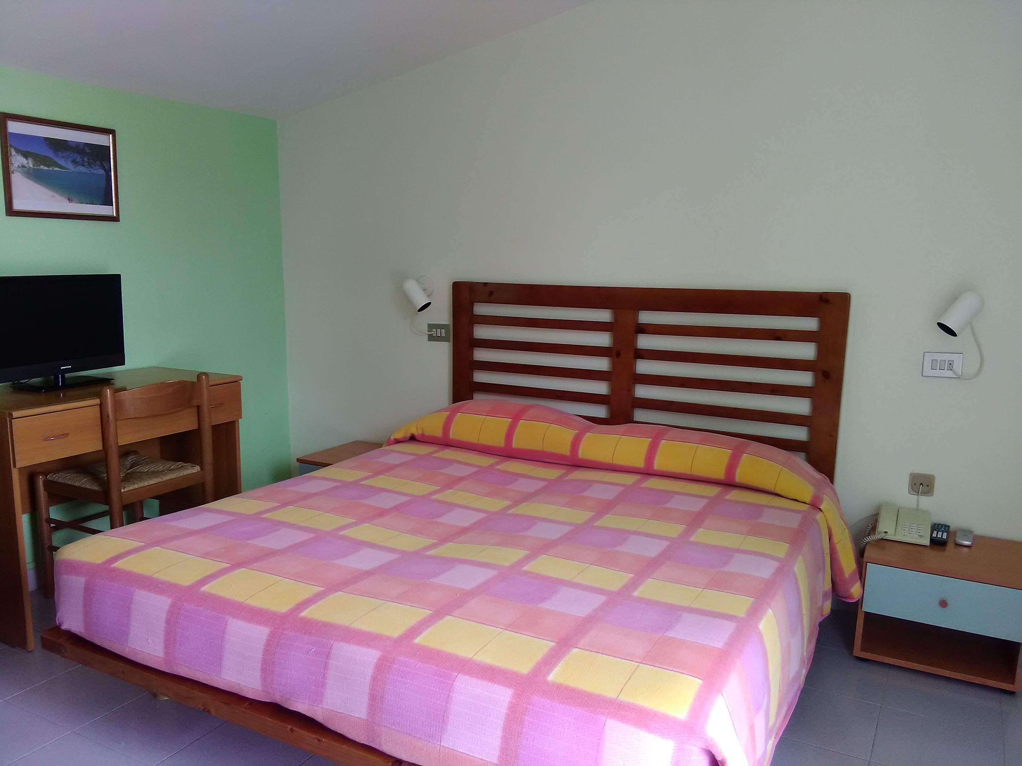Ein ordentlich eingerichtetes Schlafzimmer mit einem Bett, einem Schreibtisch und einem Fernseher.
