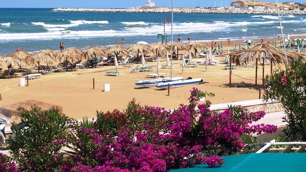 A beach with thatched umbrellas, lounge chairs, and a boat. - Vela Velo Club (Vieste)