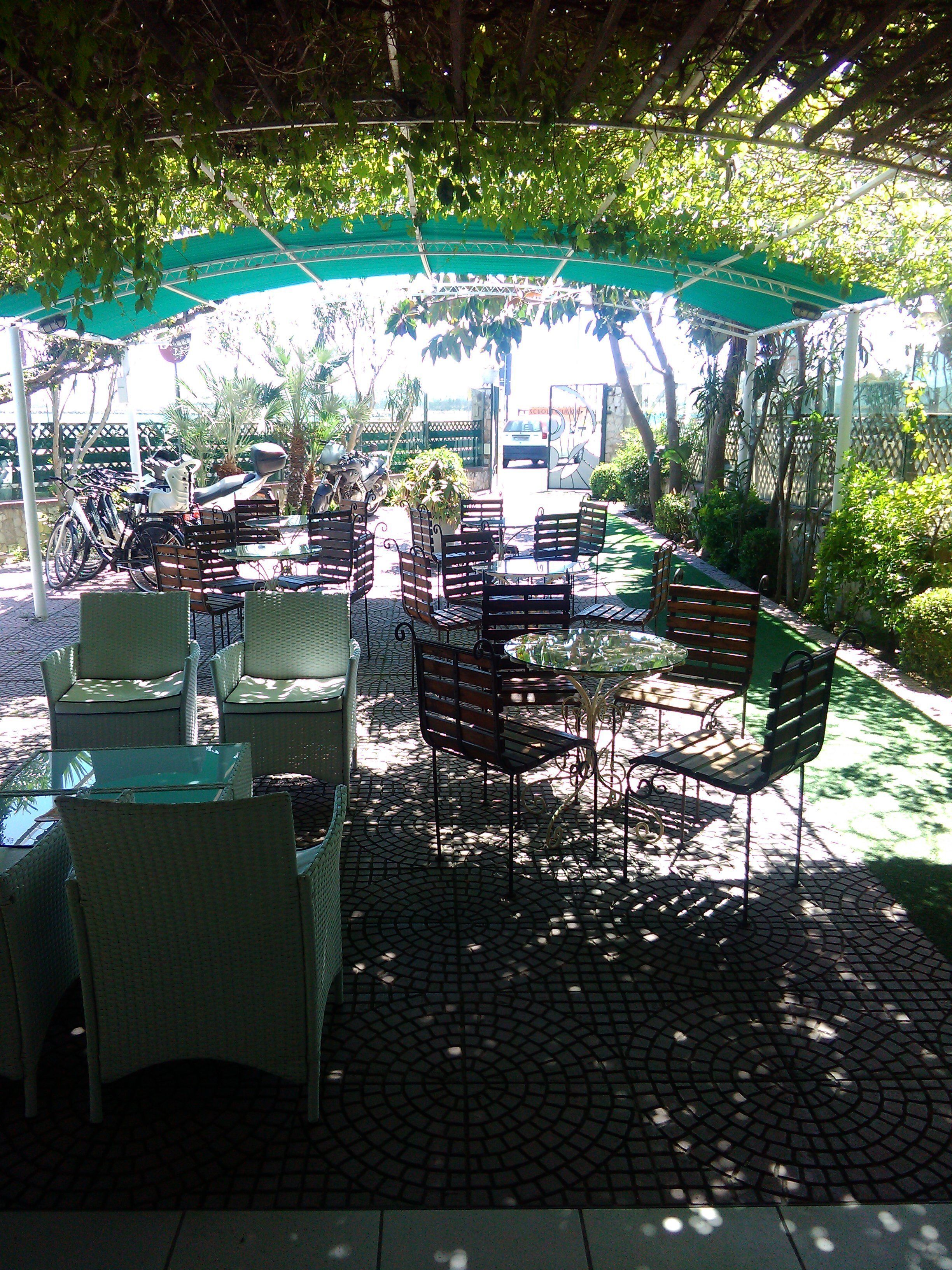 Un patio al aire libre con mobiliario de mimbre, un parasol verde y suelo de baldosas.