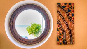 A round mirror with a view of the sea and a tree, and a patterned wall hanging. - Vela Velo Club (Vieste)