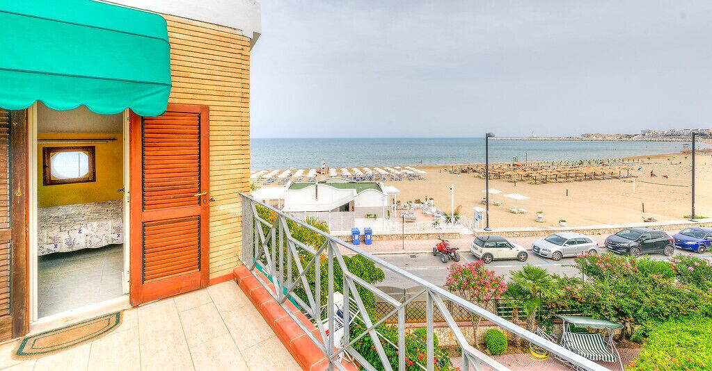 Un balcone con vista sulla spiaggia, un'area parcheggio e un piccolo giardino.
