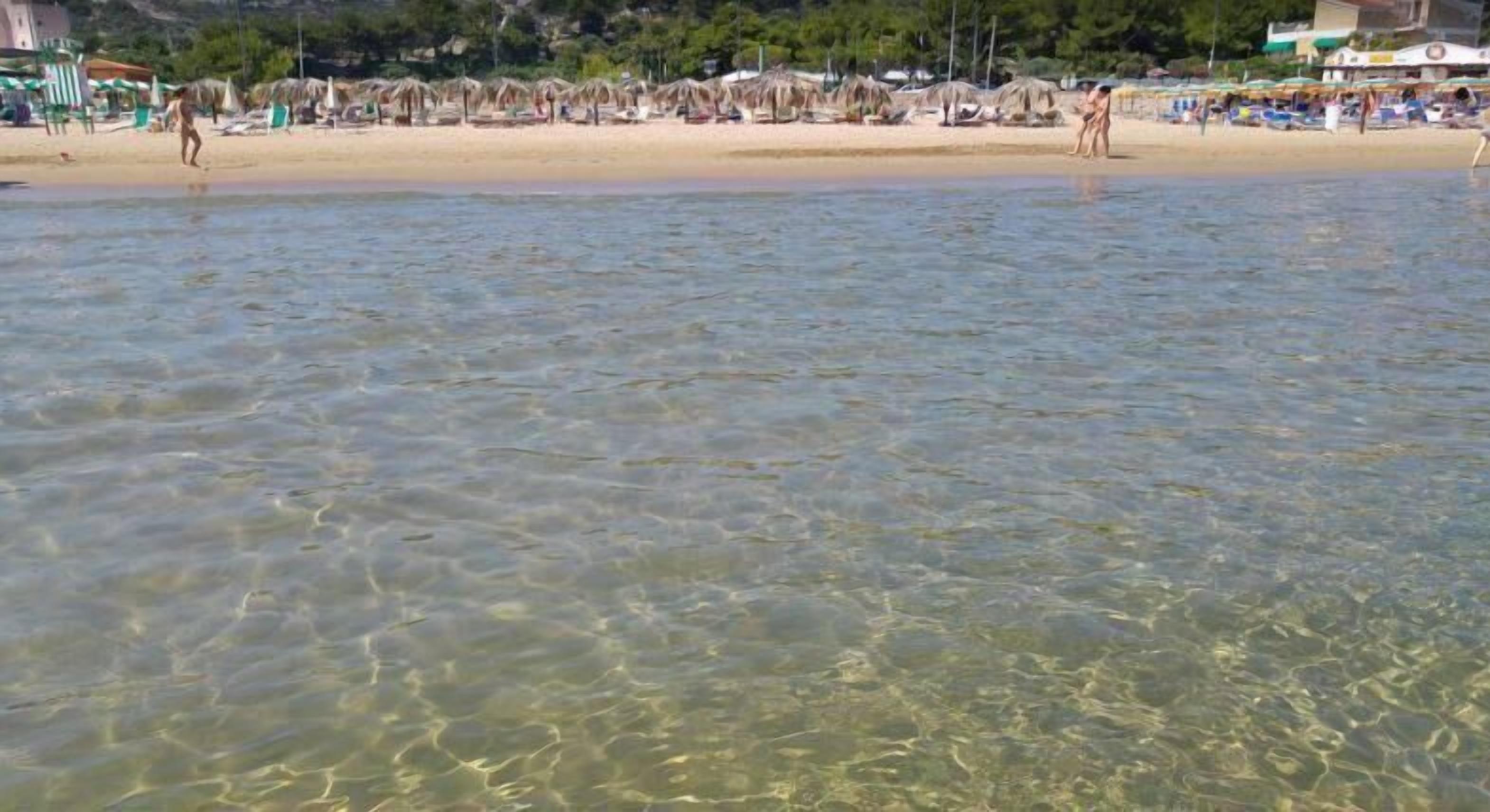 Una playa con aguas claras y poco profundas, sombrillas y sillas.