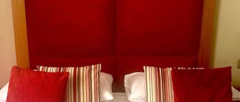 Habitación de hotel con una cama grande, cabecera roja y dos cuadros enmarcados en la pared.