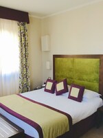 A hotel room with a large bed, a headboard, and a bedside table.