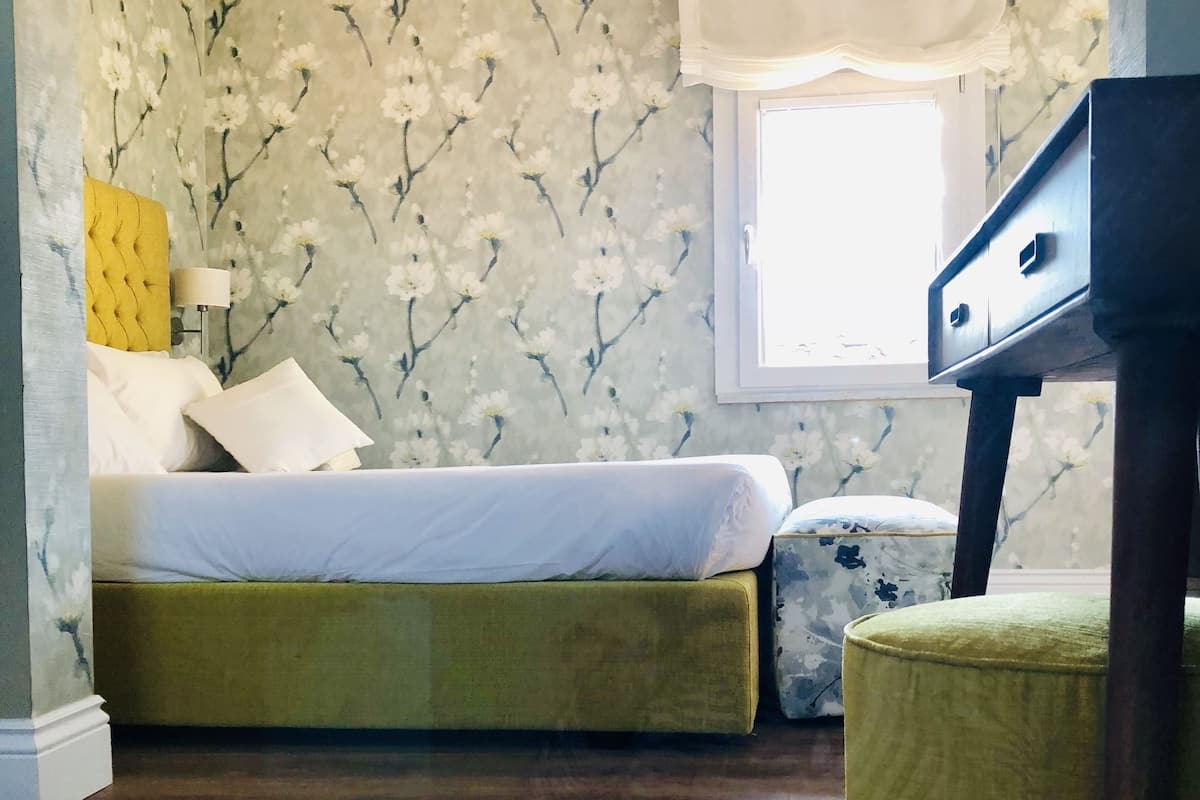 Une chambre à coucher avec un lit, une table de chevet, une lampe, une fenêtre et une commode.