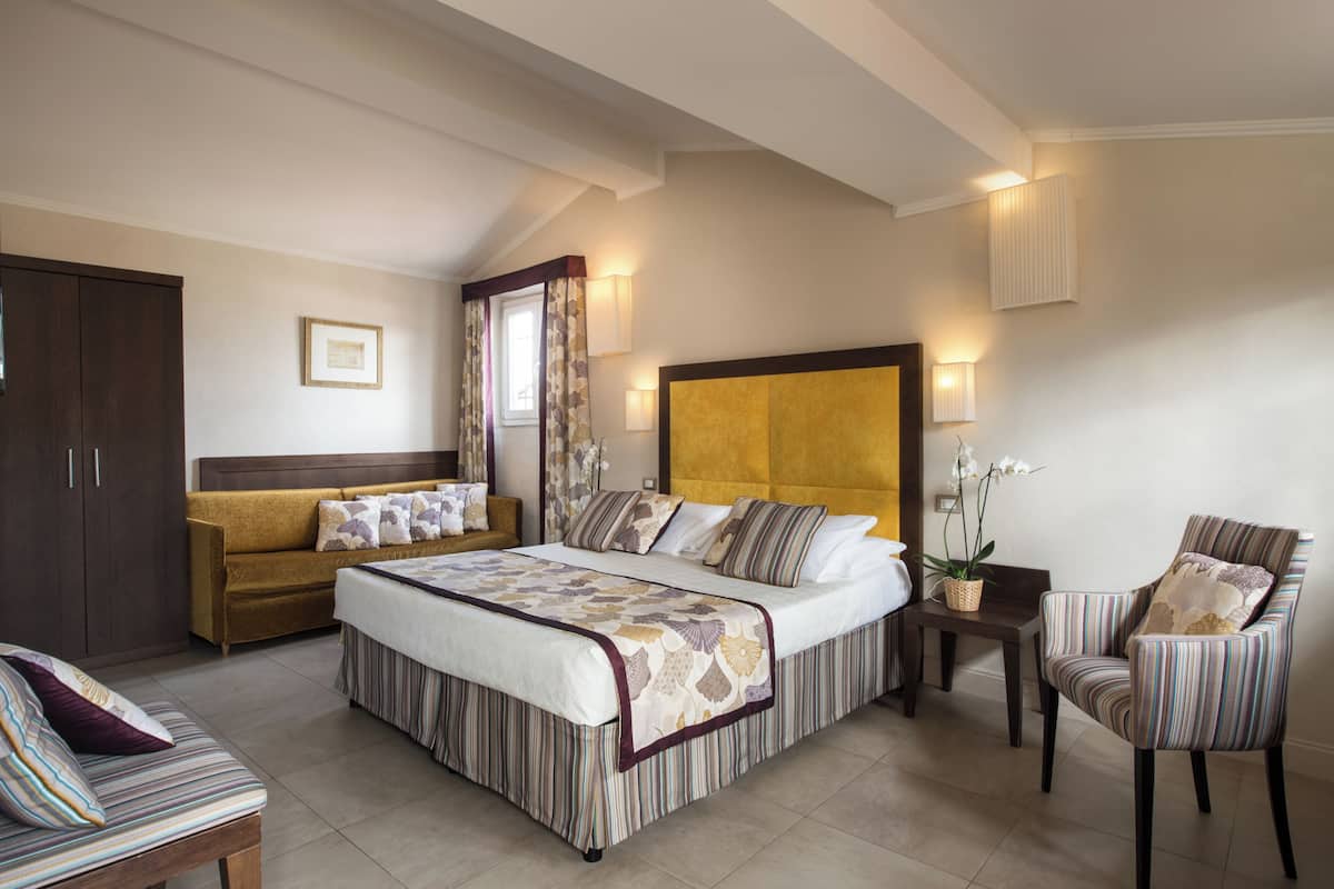 Une chambre à coucher avec un grand lit, un canapé, un fauteuil, une table de chevet et une armoire.