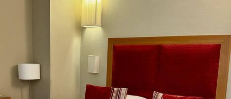 Una habitación de hotel con cama, mesita de noche, lámpara y luz empotrada en la pared.