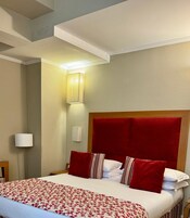 A hotel room with a bed, a nightstand, a lamp, and a wall-mounted light fixture.