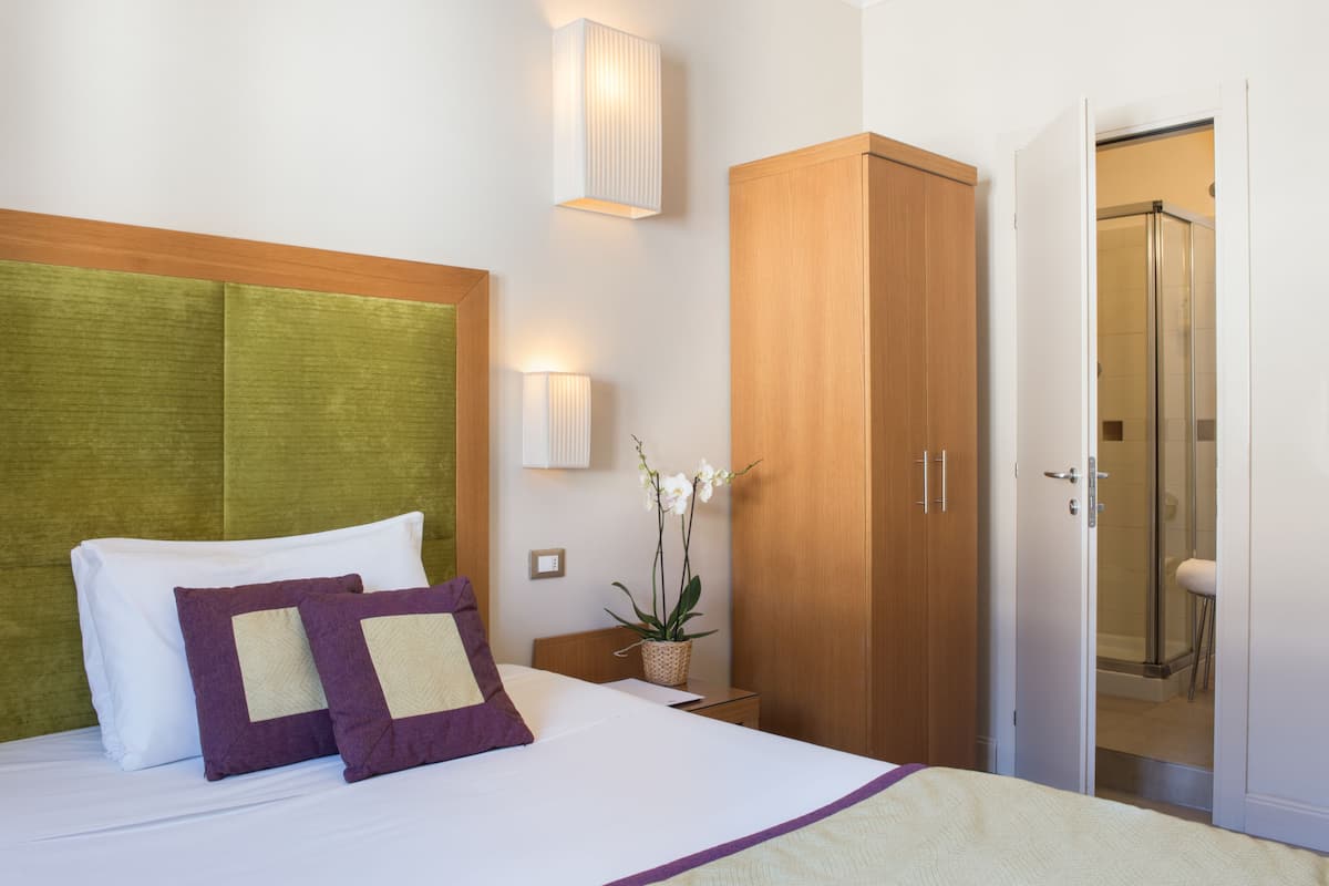 Une chambre d’hôtel avec un lit, une armoire en bois, une table de chevet, une lampe fixée au mur et une orchidée en pot.