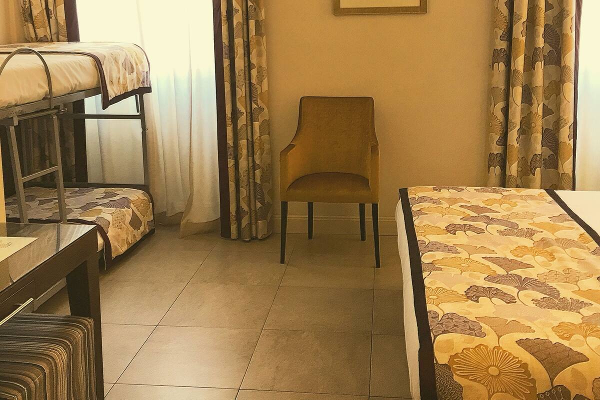 Une chambre d’hôtel avec un lit superposé, une chaise et un lit recouvert d’une courtepointe à motifs floraux.