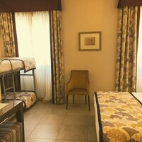 Una camera d'albergo con un letto a castello, una sedia e un letto con copriletto floreale.