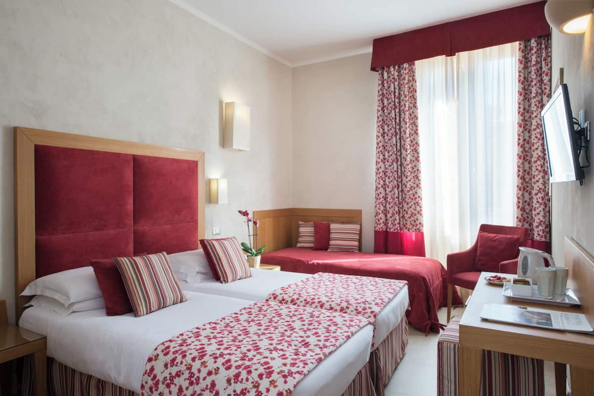 Une chambre d’hôtel avec deux lits, un bureau, une chaise et une télévision.