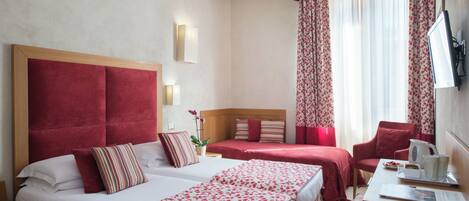 A hotel room with two beds, a desk, a chair, and a TV.