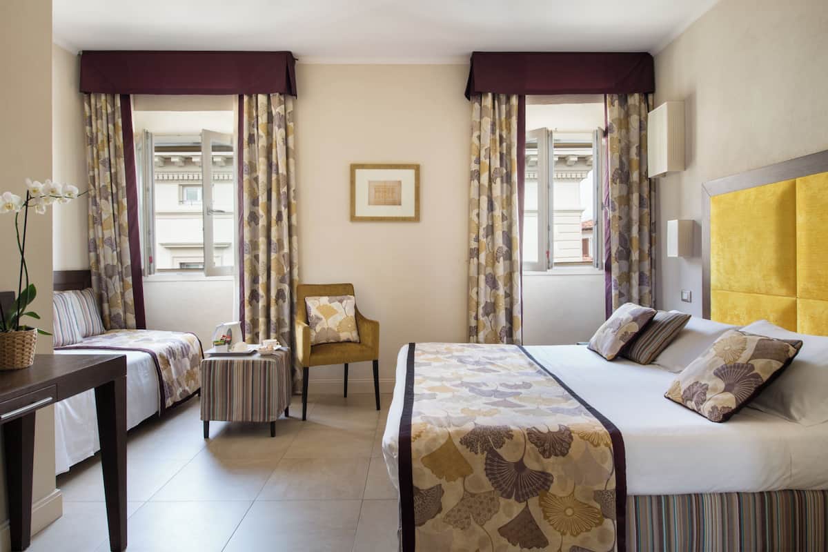Une chambre d’hôtel avec deux lits, une chaise, une petite table et une plante en pot.