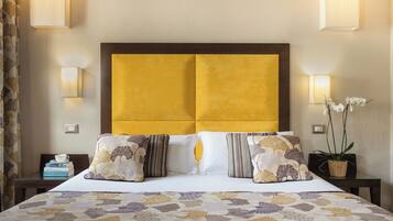 A neatly made bed with a patterned bedspread, a headboard with a yellow panel, and two bedside tables with lamps and a potted plant.