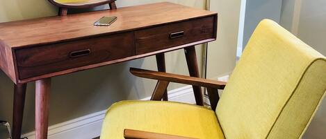 A wooden desk with a mirror, a lamp, and a yellow chair in a room with wooden flooring.