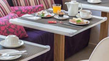Une table, des chaises et un canapé sont disposés dans une pièce dont le sol est recouvert de carreaux, créant ainsi un coin petit-déjeuner.