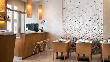 Ein modernes Café mit Holztischen, einer Theke mit einer Kaffeemaschine und einer Wanddekoration mit Vögeln und Blumen.