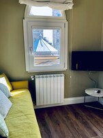 Una stanza con un letto, un termosifone, un tavolino e una finestra vista edificio.