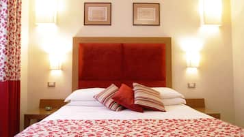 Ein Hotelzimmer mit einem großen Bett, einem roten Kopfteil, zwei gerahmten Bildern an der Wand und zwei Nachttischlampen.