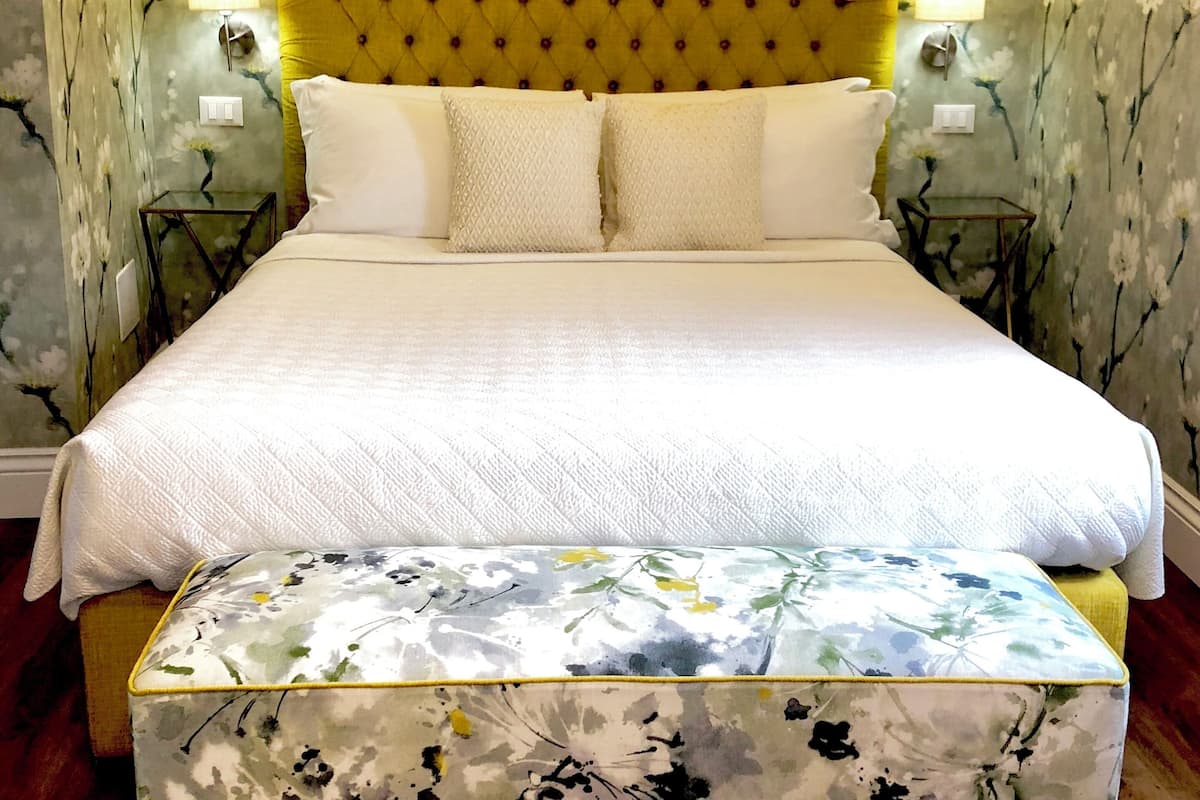 Une chambre à coucher comprenant un lit, deux tables de chevet, une petite table et un banc orné d’un motif floral.