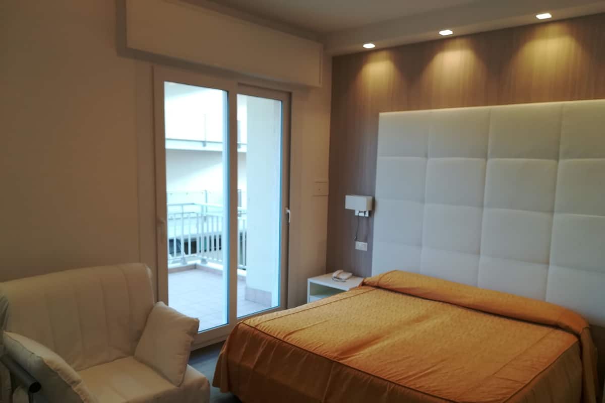 A hotel room with a bed, a chair, a nightstand, and a view of a balcony.