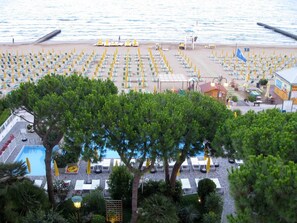 Un resort frente a la playa con filas de tumbonas y sombrillas, un área de piscina y un edificio con un letrero.