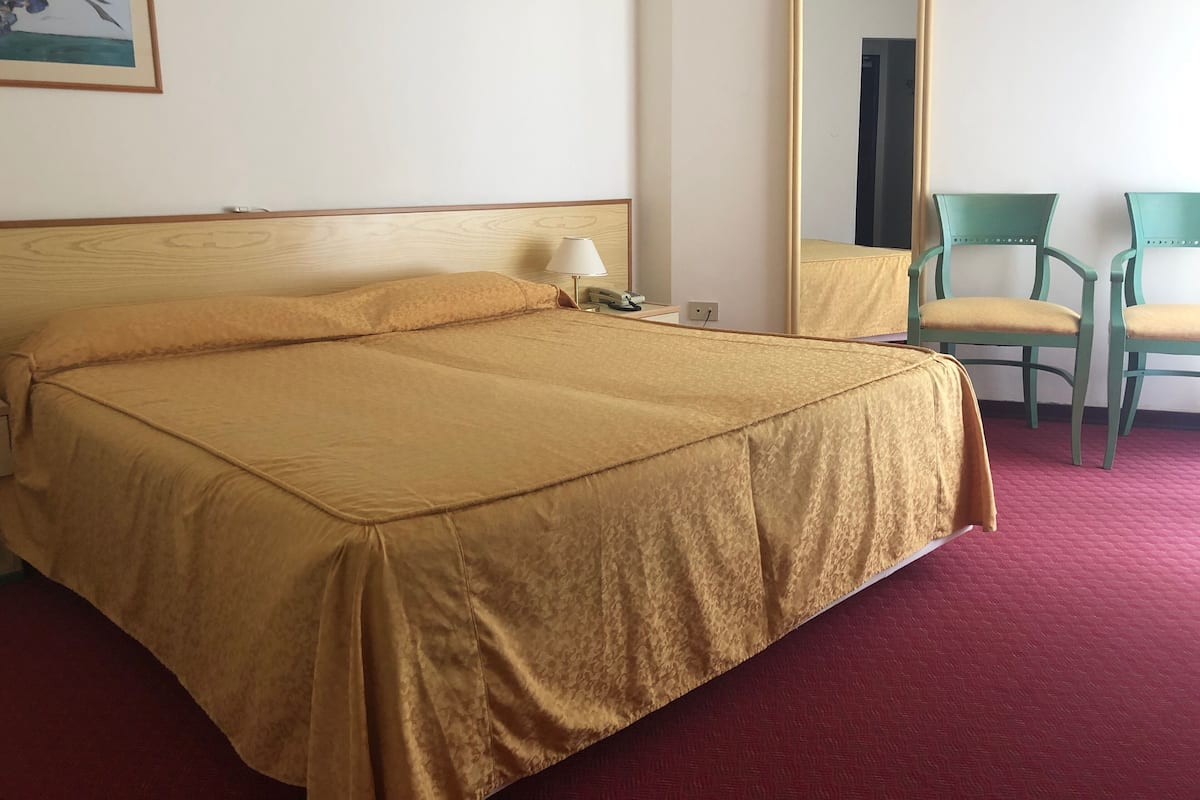 A hotel room with a bed, a bedside lamp, a mirror, and a chair.