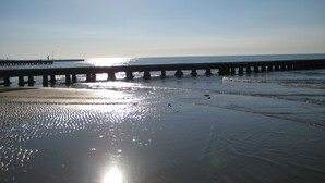 A beach with a pier extending into the water, reflecting the sun.