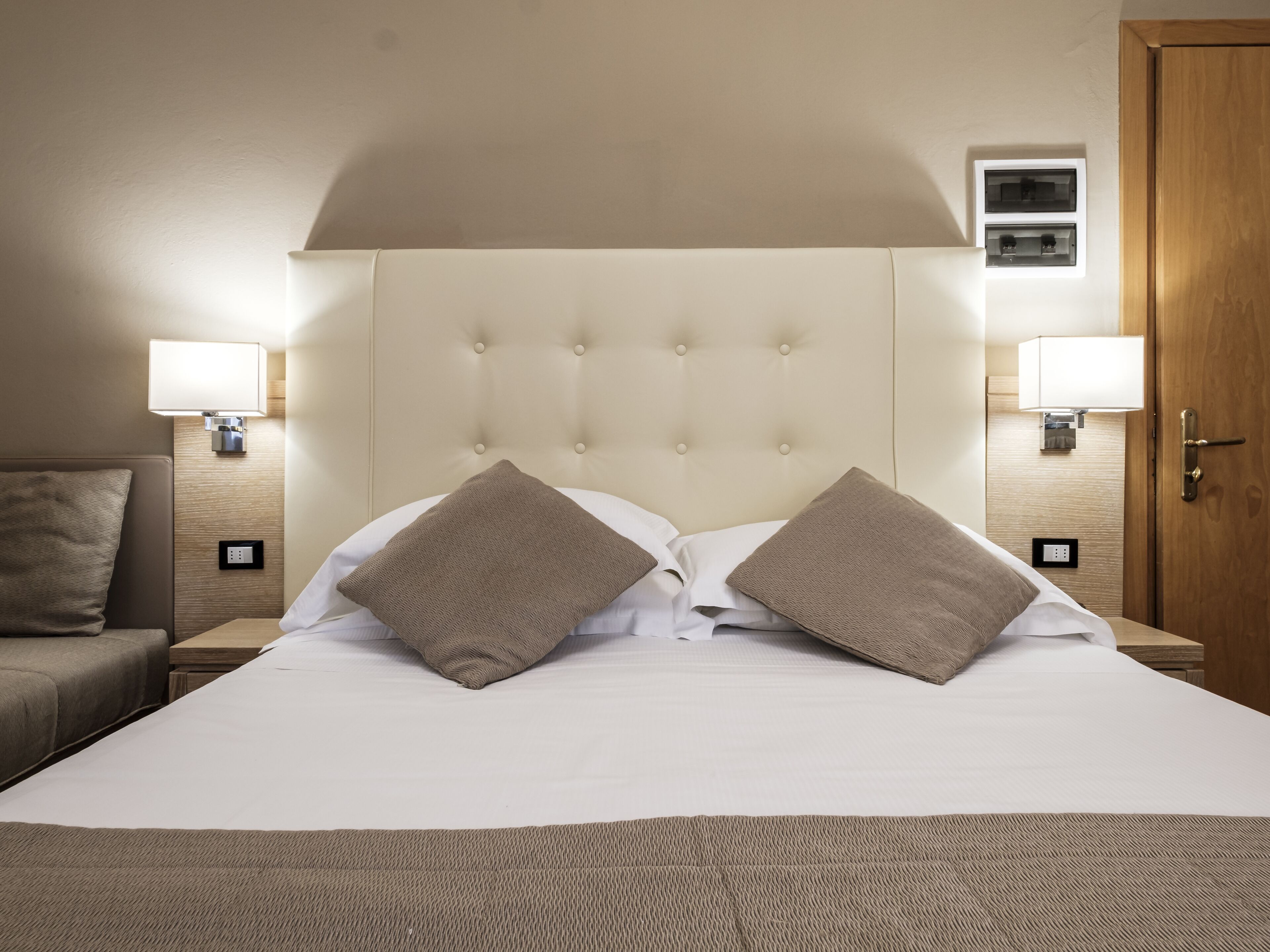 Un letto rifatto con due cuscini, un comodino con una lampada e una porta in legno.