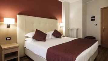 Ein Hotelzimmer mit einem großen Bett, zwei Nachttischlampen, einem Holznachttisch, einem Heizkörper und einer Tür.