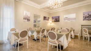Comedor con mesas y sillas redondas, una araña y obras de arte colgadas en la pared.