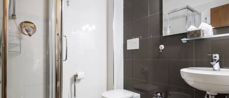 A modern bathroom with a glass shower enclosure, a toilet, a bidet, and a sink with a mirror above.