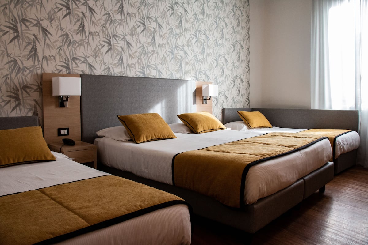A hotel room with two beds, each with a headboard, bedside tables, lamps, and a floral wallpaper design.