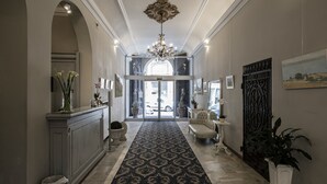 Un amplio pasillo con alfombra estampada, un candelabro y una recepción con cuadros enmarcados.