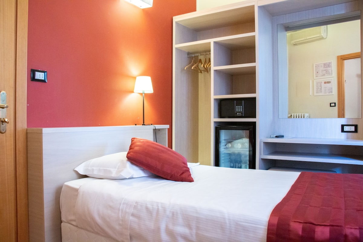 A hotel room with a bed, a wardrobe, a mirror, and a lamp.