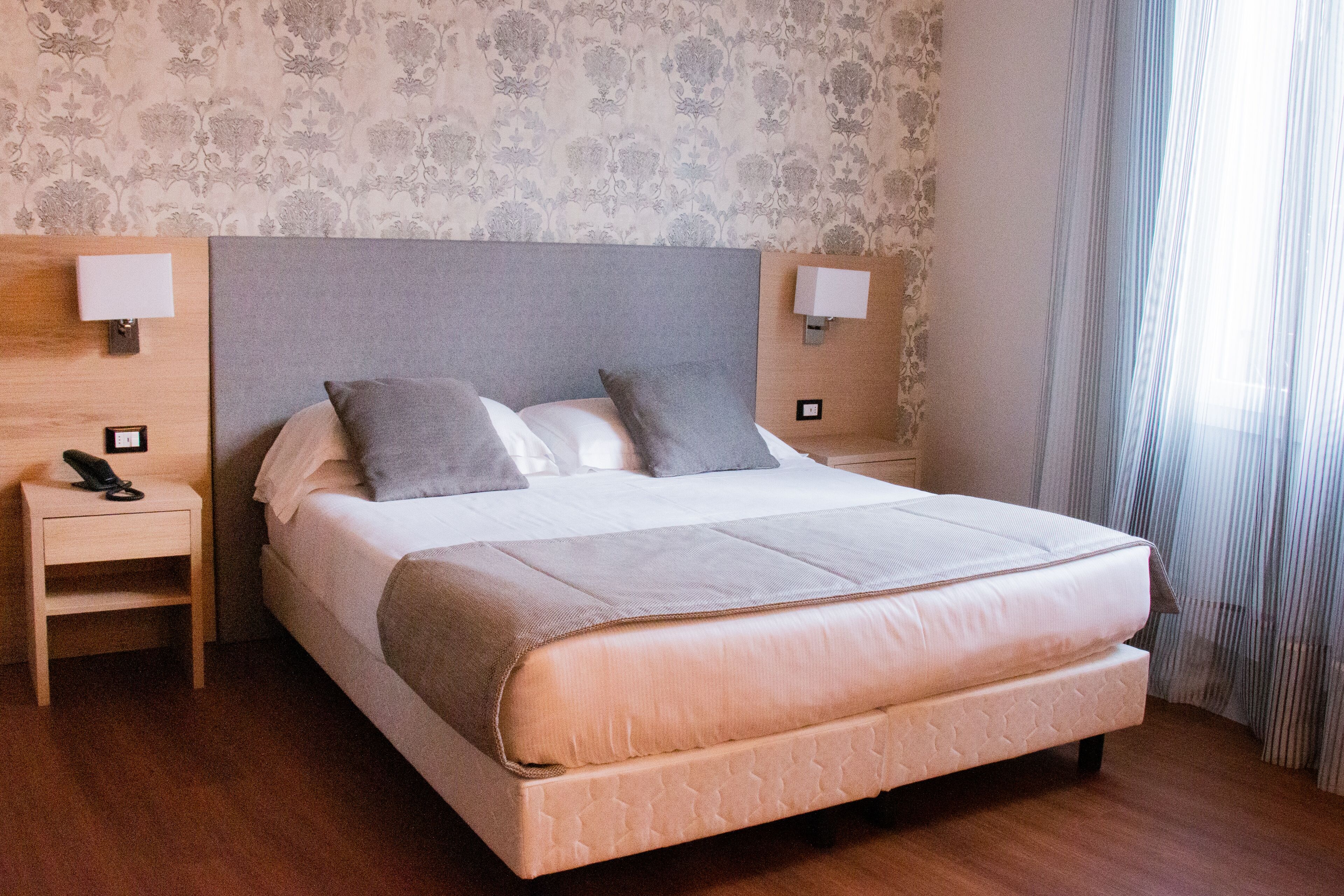 A double bed with a grey headboard, two bedside lamps, a bedside phone, and a wooden nightstand.