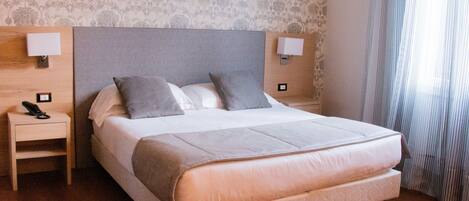 A double bed with a grey headboard, two bedside lamps, a bedside phone, and a wooden nightstand.