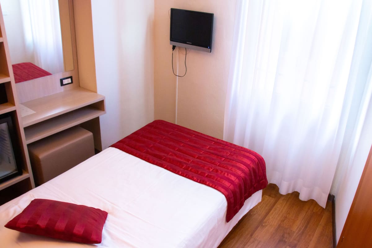 A hotel room with a bed, a TV mounted on the wall, and a wooden floor.