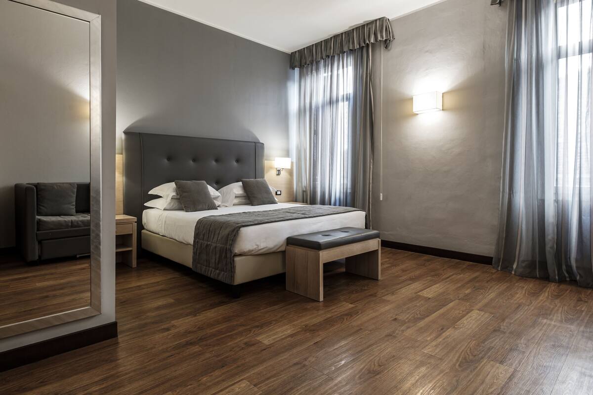 A modern bedroom with a large bed, a nightstand, a bench, and a sofa.