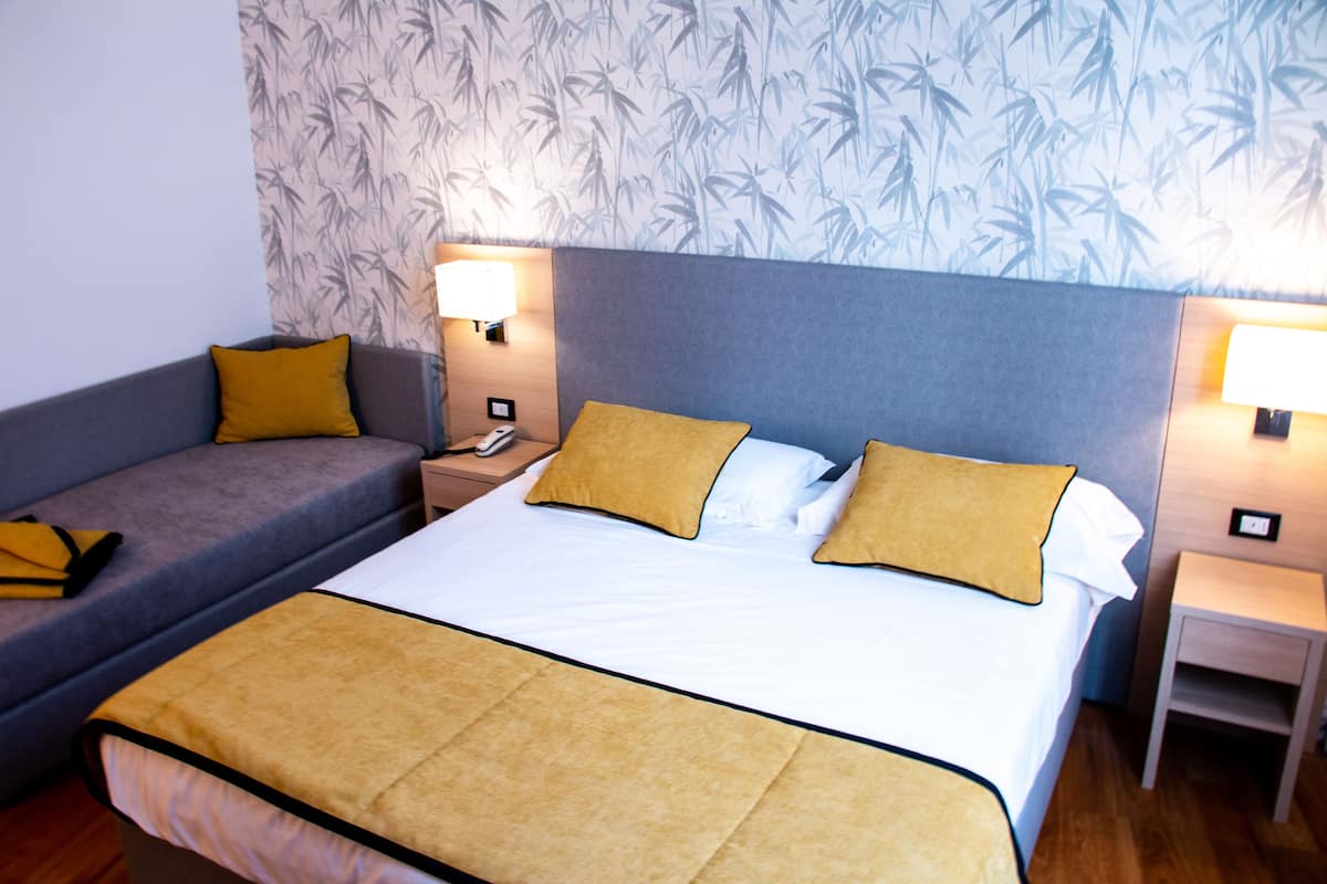 A hotel room with a bed, a sofa, two nightstands, and a wall with a bamboo pattern.